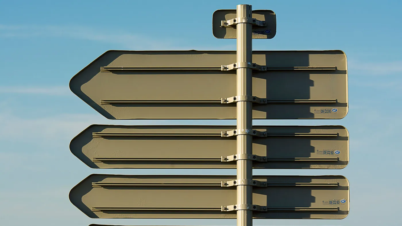 A signpost photographed from behind against a blue sky, every direction blade blank with nothing written on it.