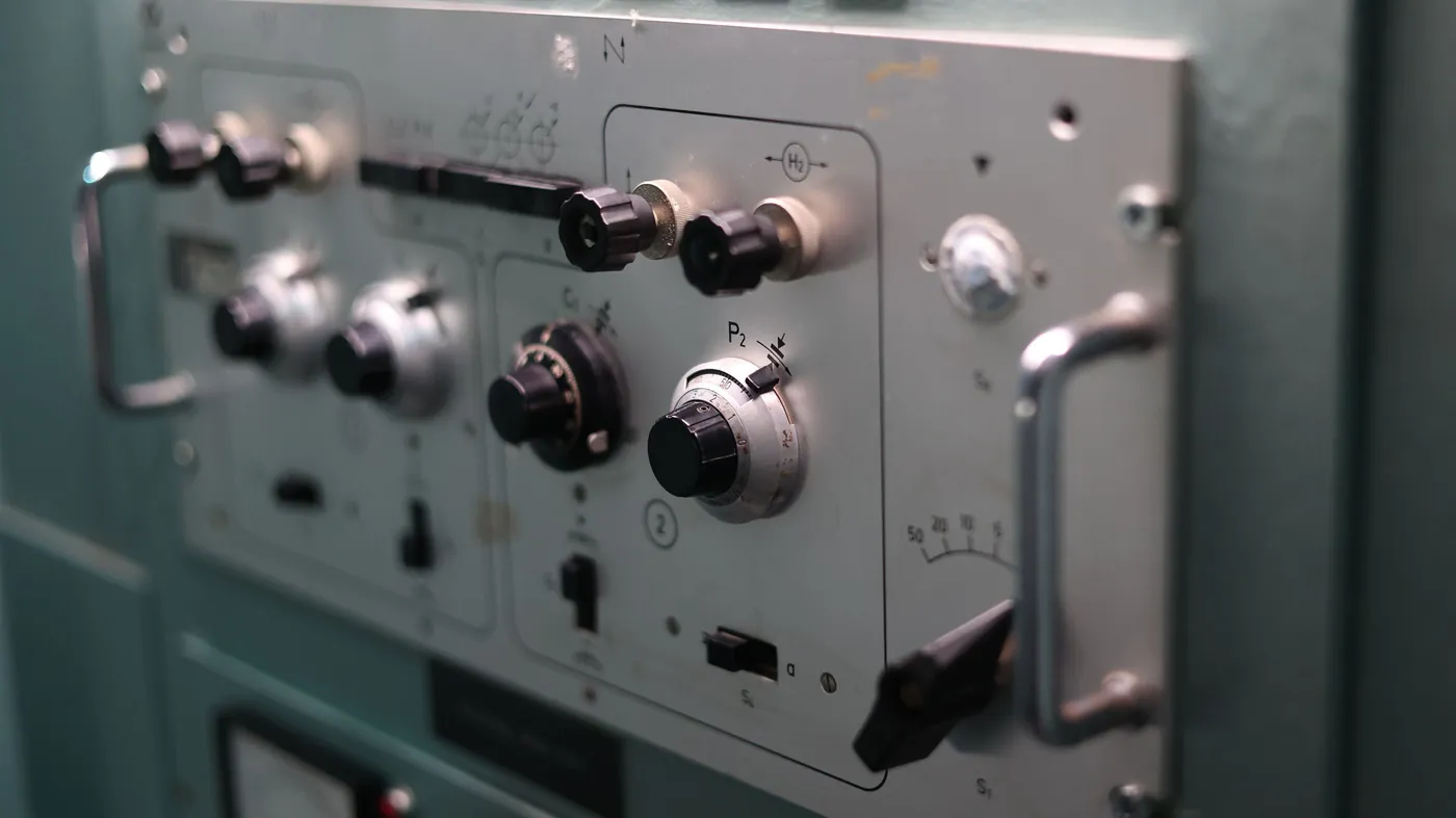 A close-up of a grey industrial control panel with labelled dials, toggles and switches, each one a deliberate, separate control.