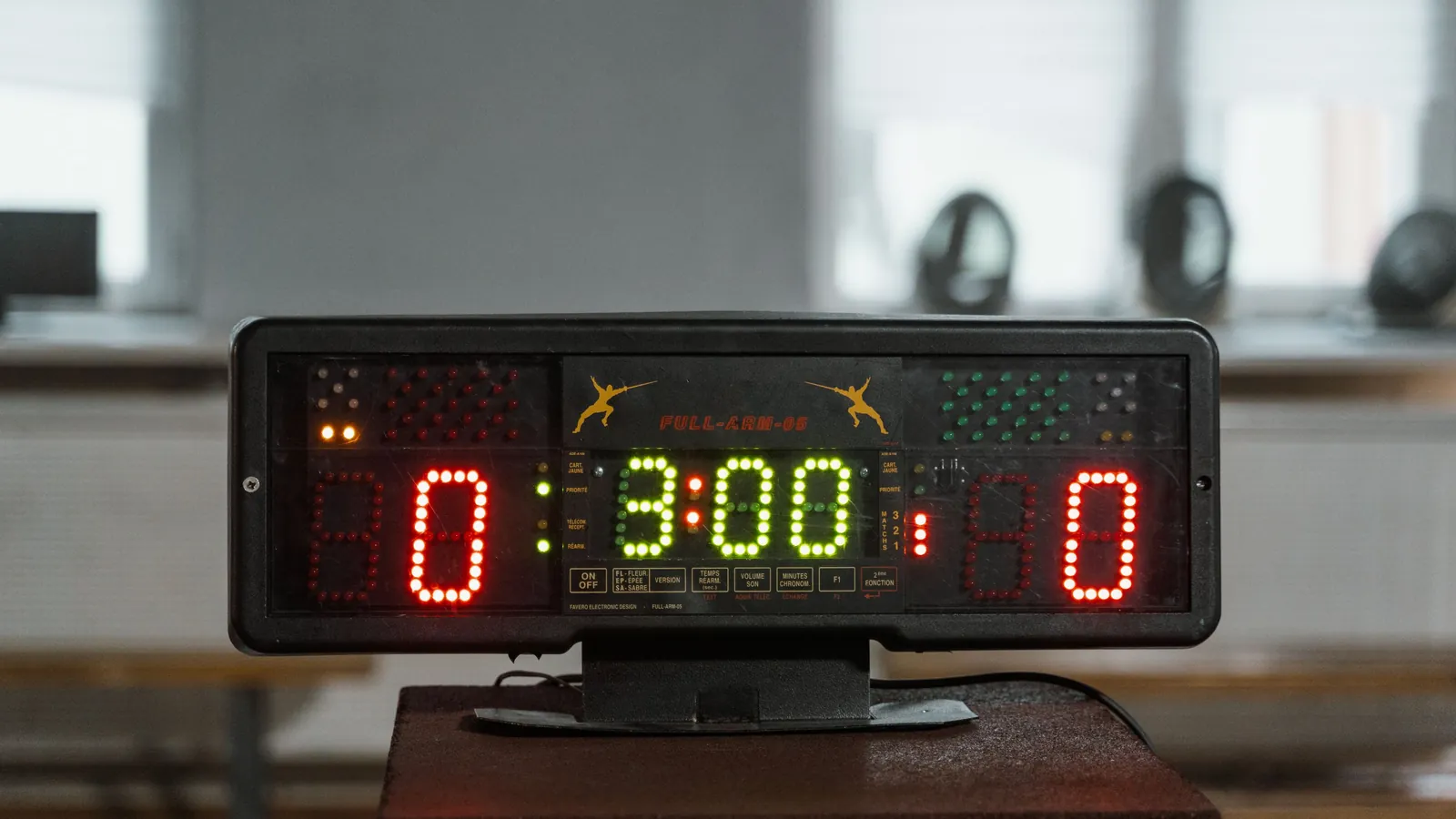An electronic scoreboard on a stand in an empty hall, both sides lit up showing a score of zero.