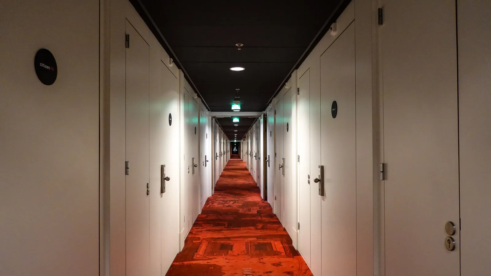 A long, symmetrical hotel corridor lined with closed white doors under warm ceiling lights.
