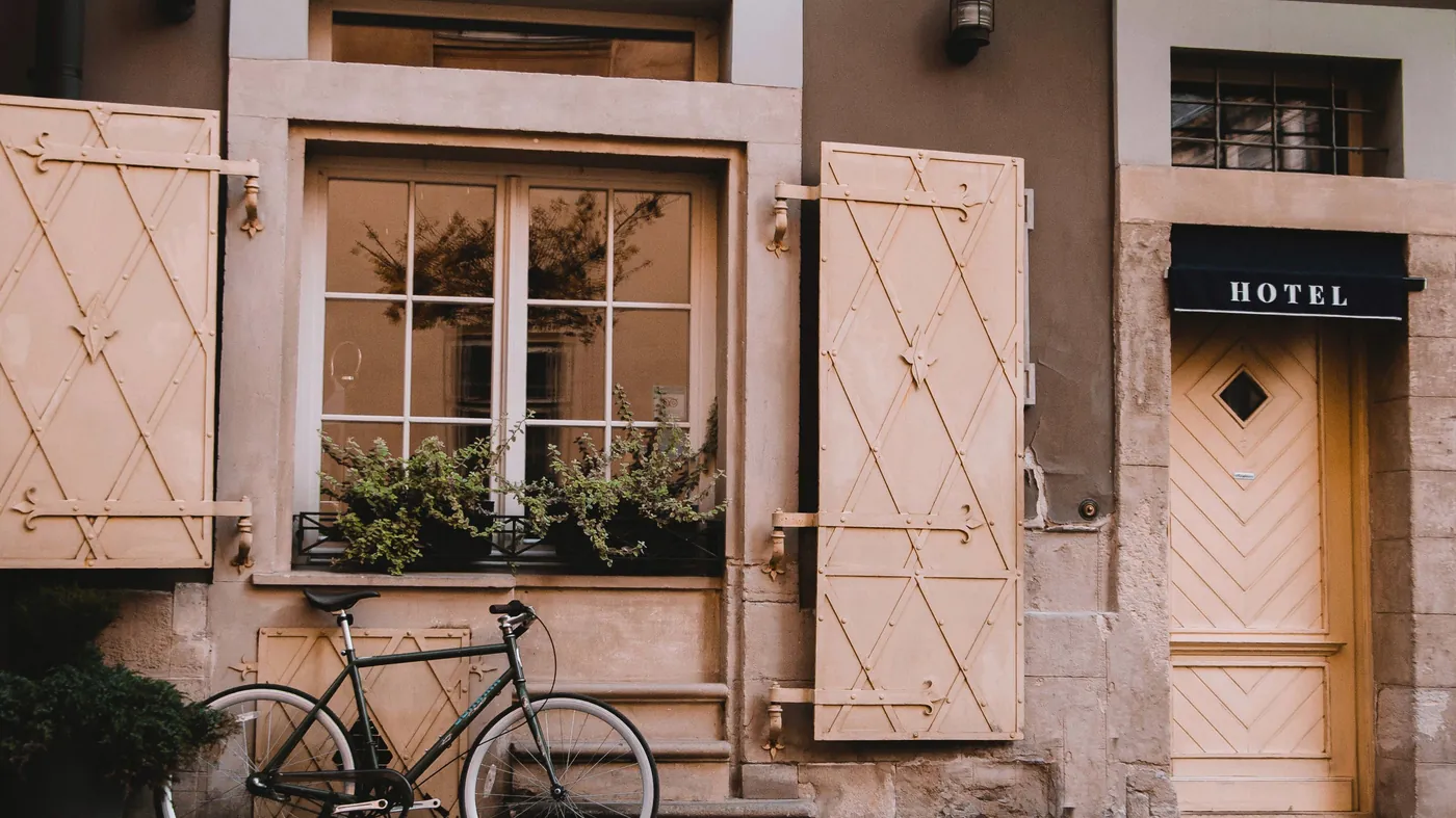 The facade of a small independent hotel on a quiet street, with a bicycle parked under a shuttered window.
