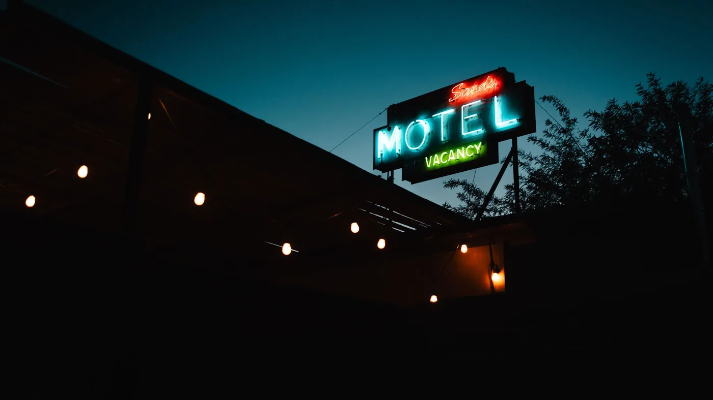 A vintage neon motel sign glowing at dusk with the word vacancy lit up beside an empty road.