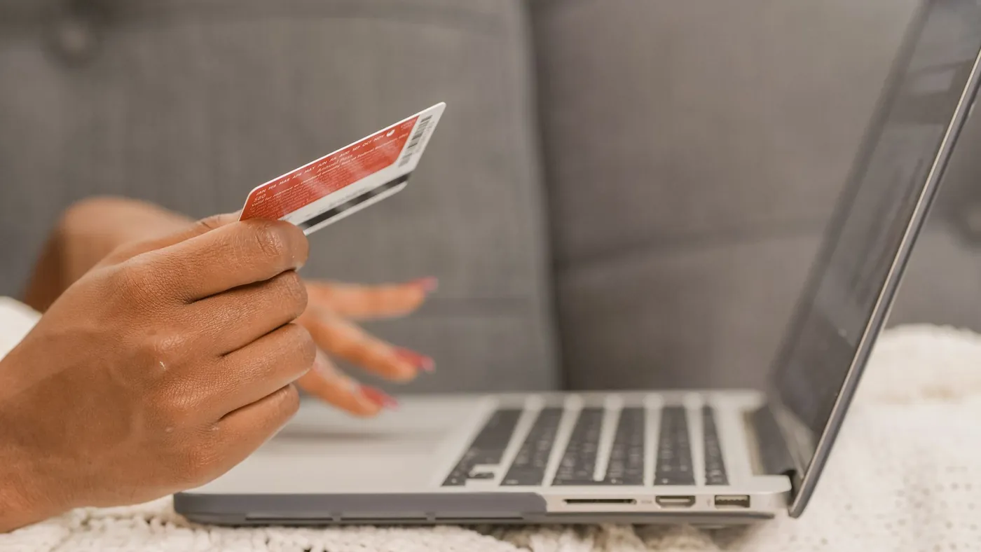 A person holding a red payment card in one hand while typing on a laptop keyboard with the other.