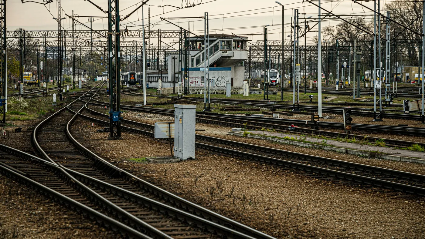 A wide railway junction with several tracks curving past a signal box under overhead power lines.