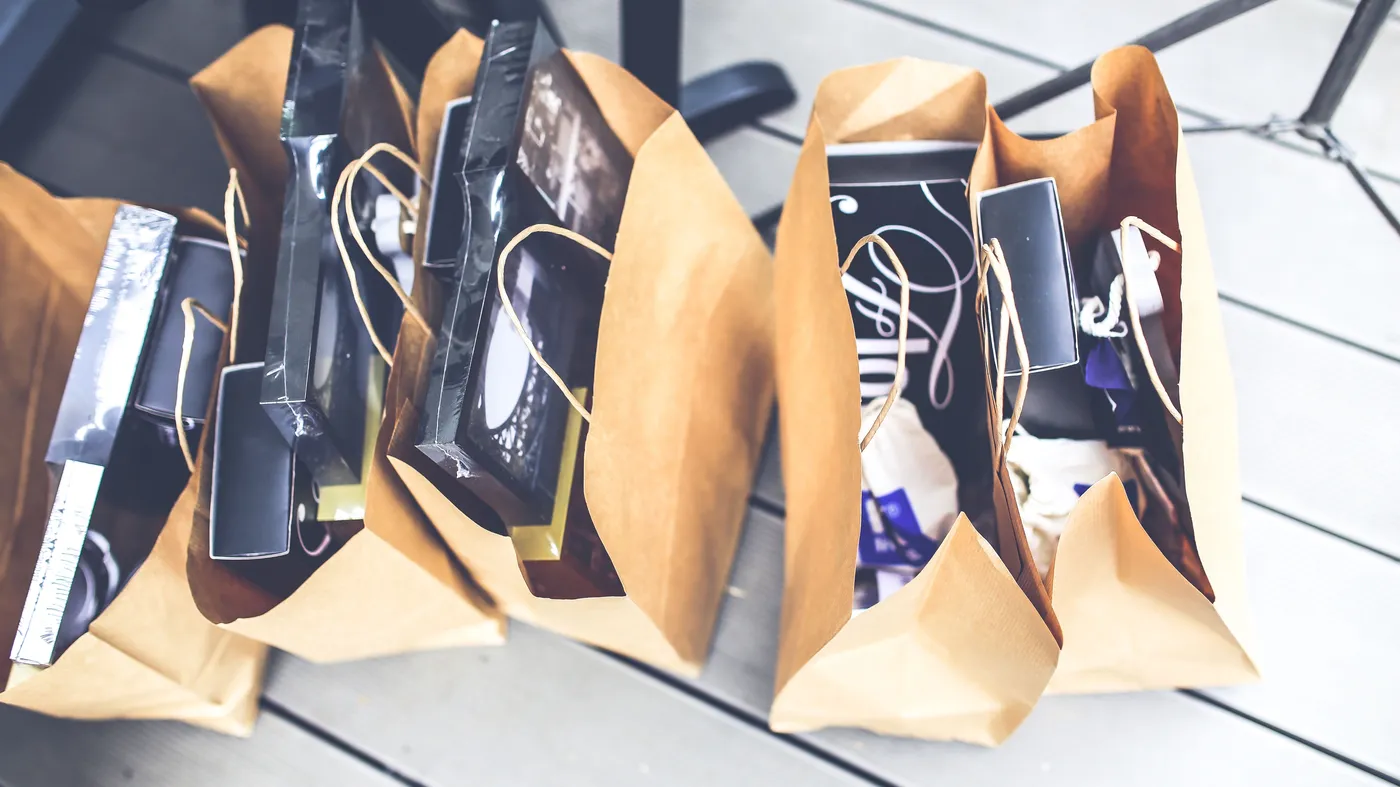 Seen from above, a row of brown paper shopping bags filled with boxed goods stands on a light wooden floor.